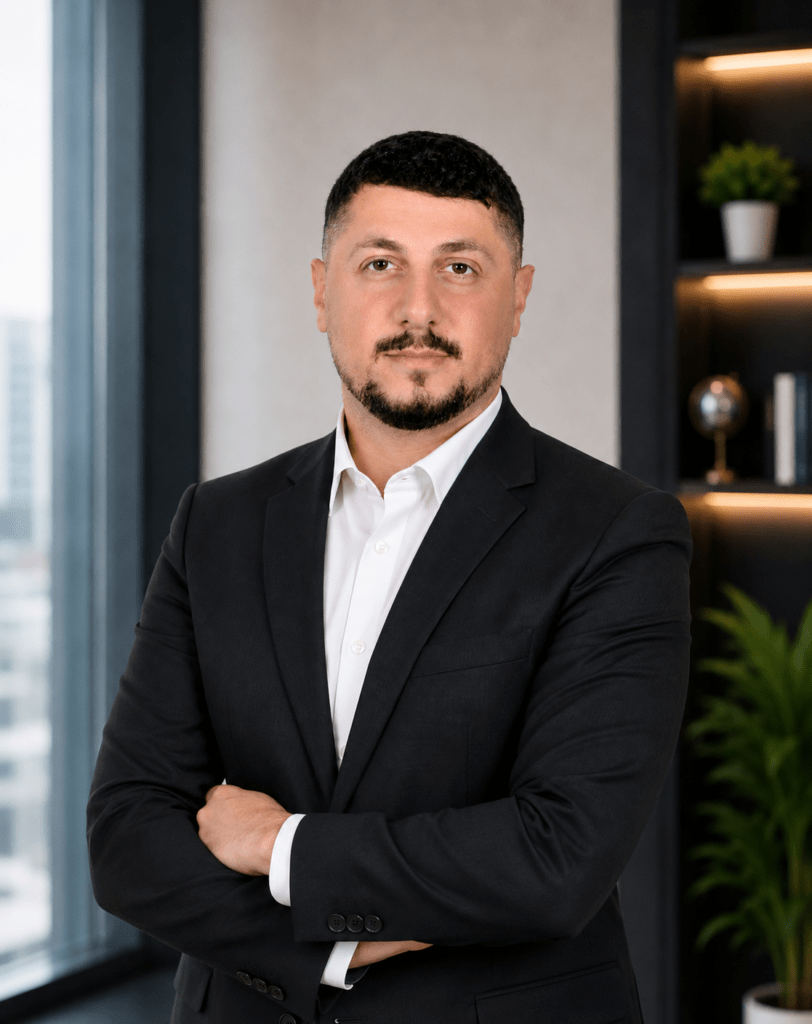 Professional portrait of Georges Samia, Associate Director of Business Development at MEmob, standing with folded arms in a modern office.